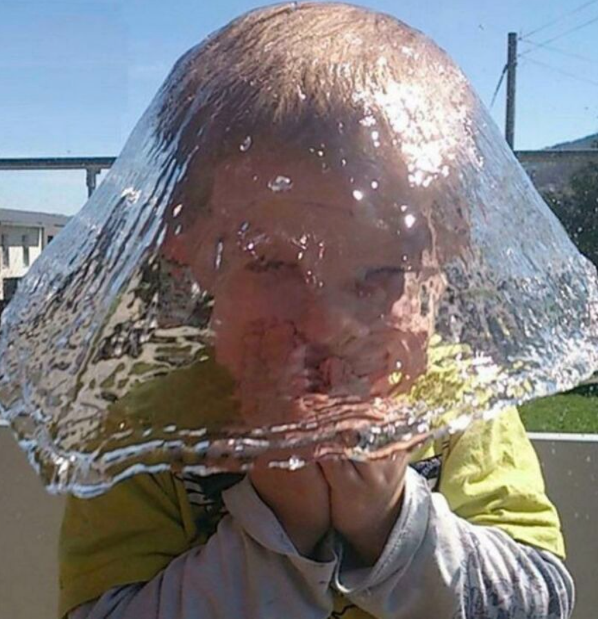 Detská tvár schovaná za priehľadnou, zmrznutou vodou, na slnečnom dni vonku.