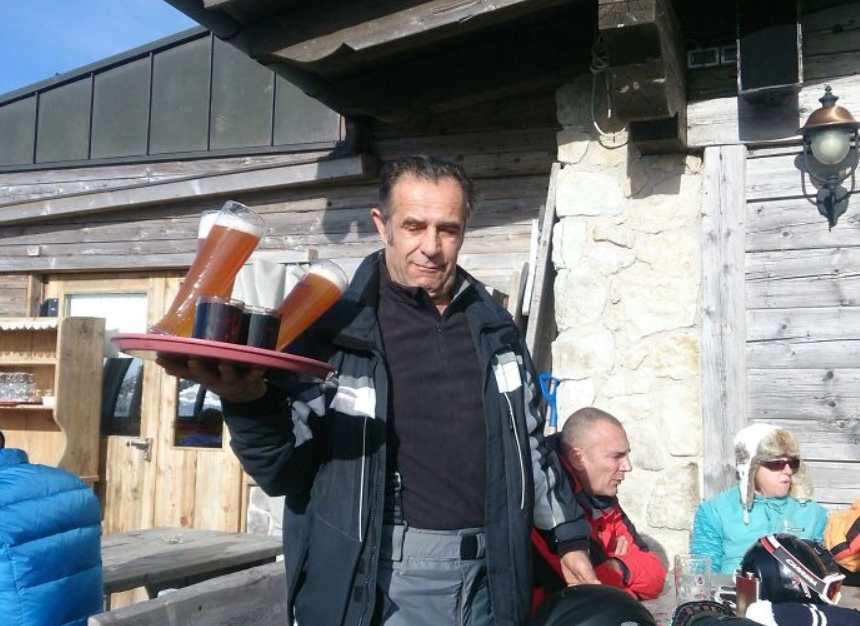 Osoba podáva tácku s pivami na horskej chate za slnečného dňa.