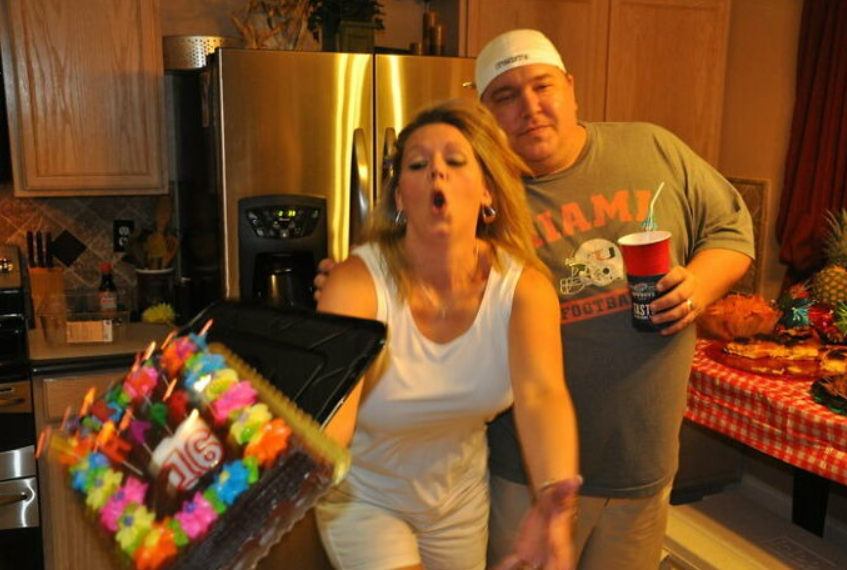 Žena v kuchyni omylom púšťa narodeninovú tortu z rúk, zatiaľ čo muž so smiechom sleduje situáciu.