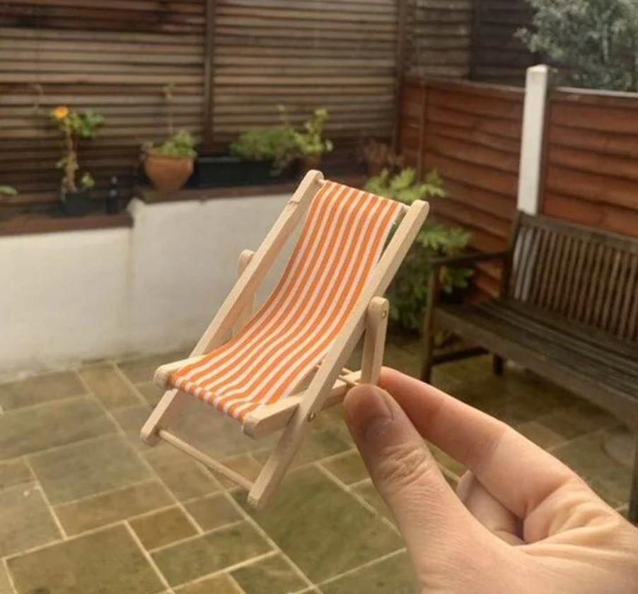 Miniatúrne ležadlo s oranžovými pruhmi držané v ruke na terase.