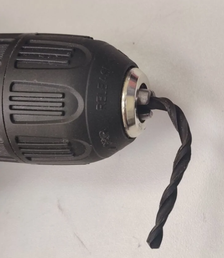 Čierna vŕtačka s vrtákom na bielom pozadí, detailný pohľad na vrták upnutý do kovového skľučovadla.