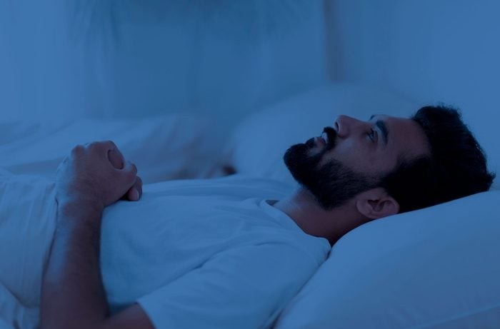 Muž leží v posteli a nespí, nočná scéna s modrým osvetlením, premýšľa alebo má problémy so zaspávaním.