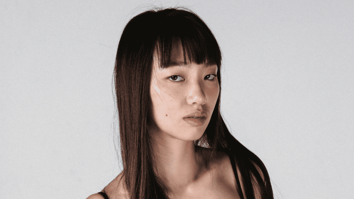 Mladá žena s dlhými vlasmi pozerá smerom do objektívu na neutrálnom pozadí.