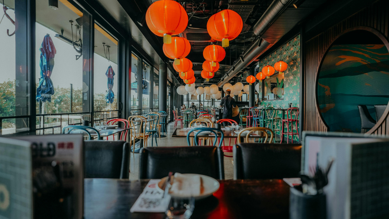 Moderná reštaurácia so sedením a farebnými lampiónmi, pripravená na hostí, s výhľadom na terasu.