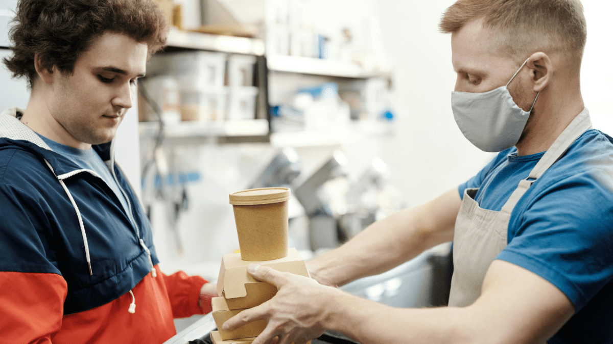 Doručenie jedla: Muž odovzdáva zákazníkovi balík s kávou a jedlom v reštaurácii s rýchlym občerstvením.