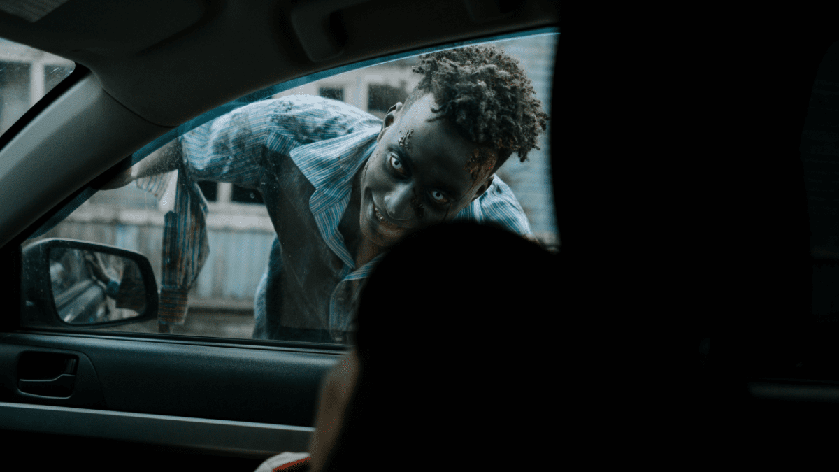 Osoba s Halloweenovým makeupom nakúka do auta cez okno, výraz tajomný a strašidelný.