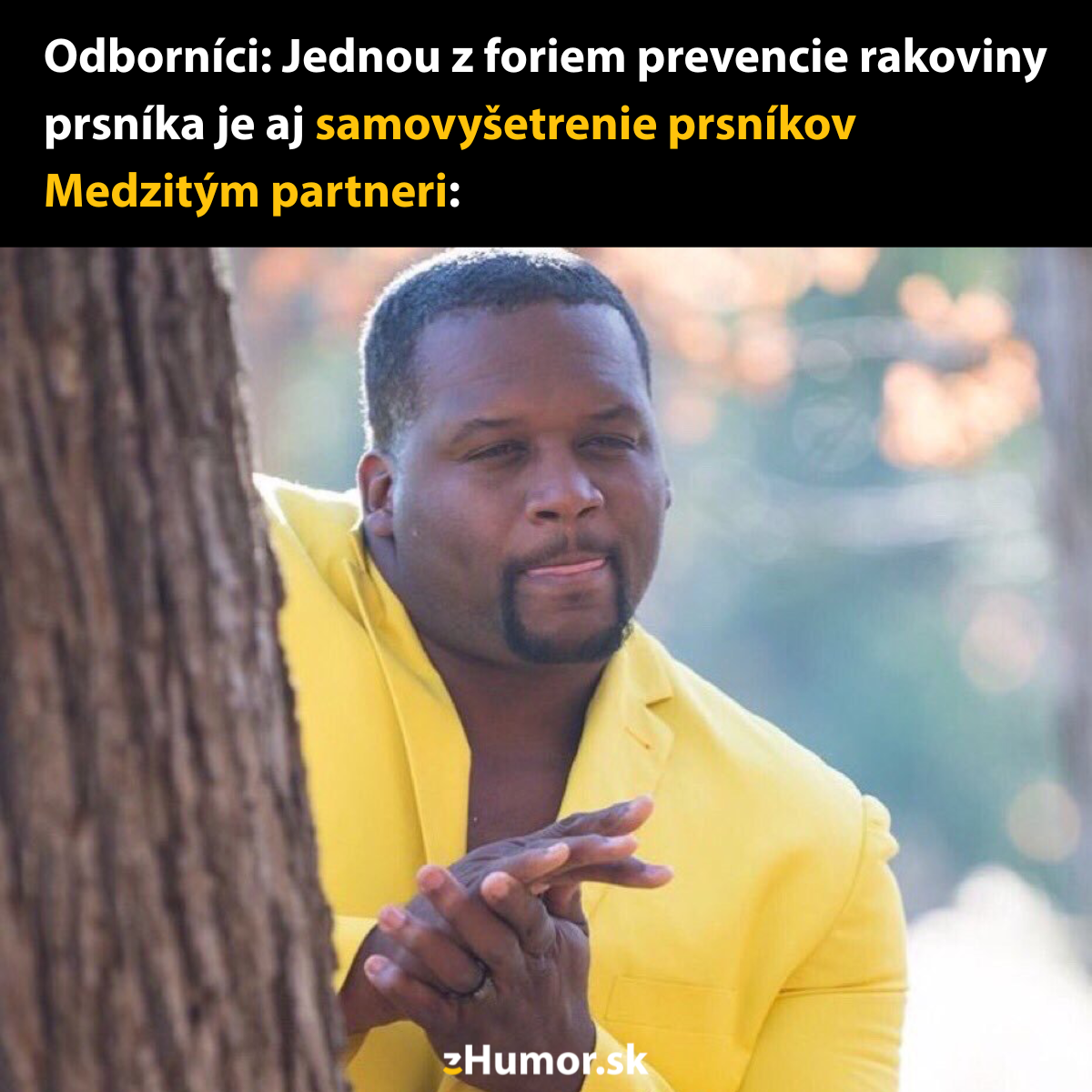 Muž v žltom saku stojí pri strome a ruky si trie s úsmevom, humor o samovyšetrení prsníkov.