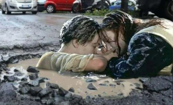 Pár vo vode uprostred výmoľu na ceste, kreatívne zobrazenie romantiky v nečakanom prostredí.