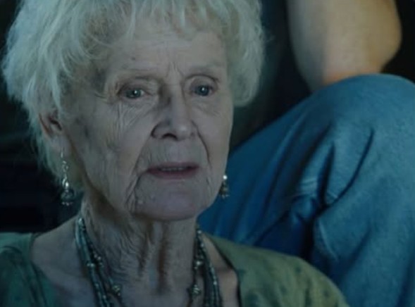 Loď cez staré ženy rozpráva svoj príbeh, oblečená v zelenom s náušnicami a náhrdelníkom, sediac vedľa niekoho v modrých džínsach.