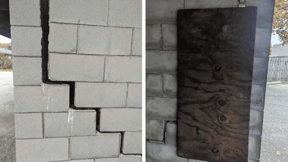 Prasknutá tehlová stena vedľa opravy drevenou doskou vonku.