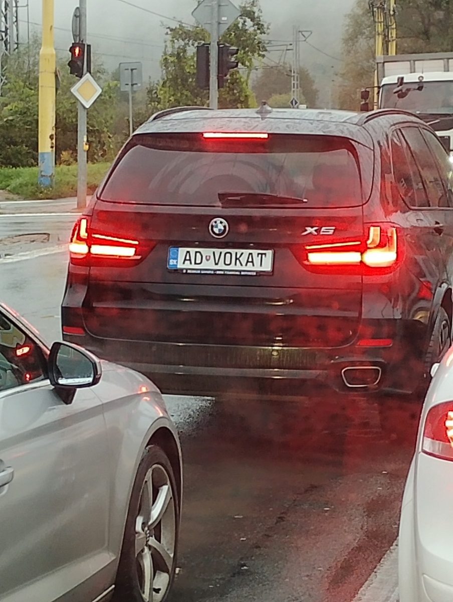 Čierne BMW X5 s poznávacou značkou „ADVOKAT“ na križovatke, čakanie na semafore.