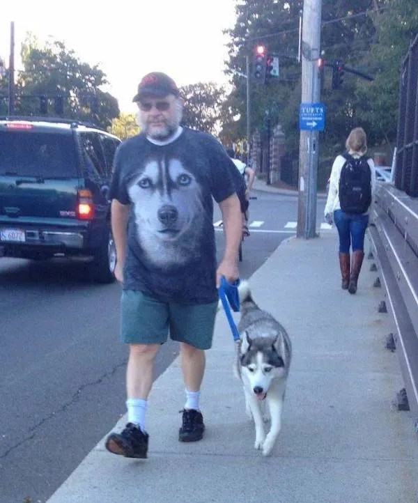 Muž na prechádzke so psom husky, nosí tričko s veľkým obrázkom huskyho na ceste v meste.