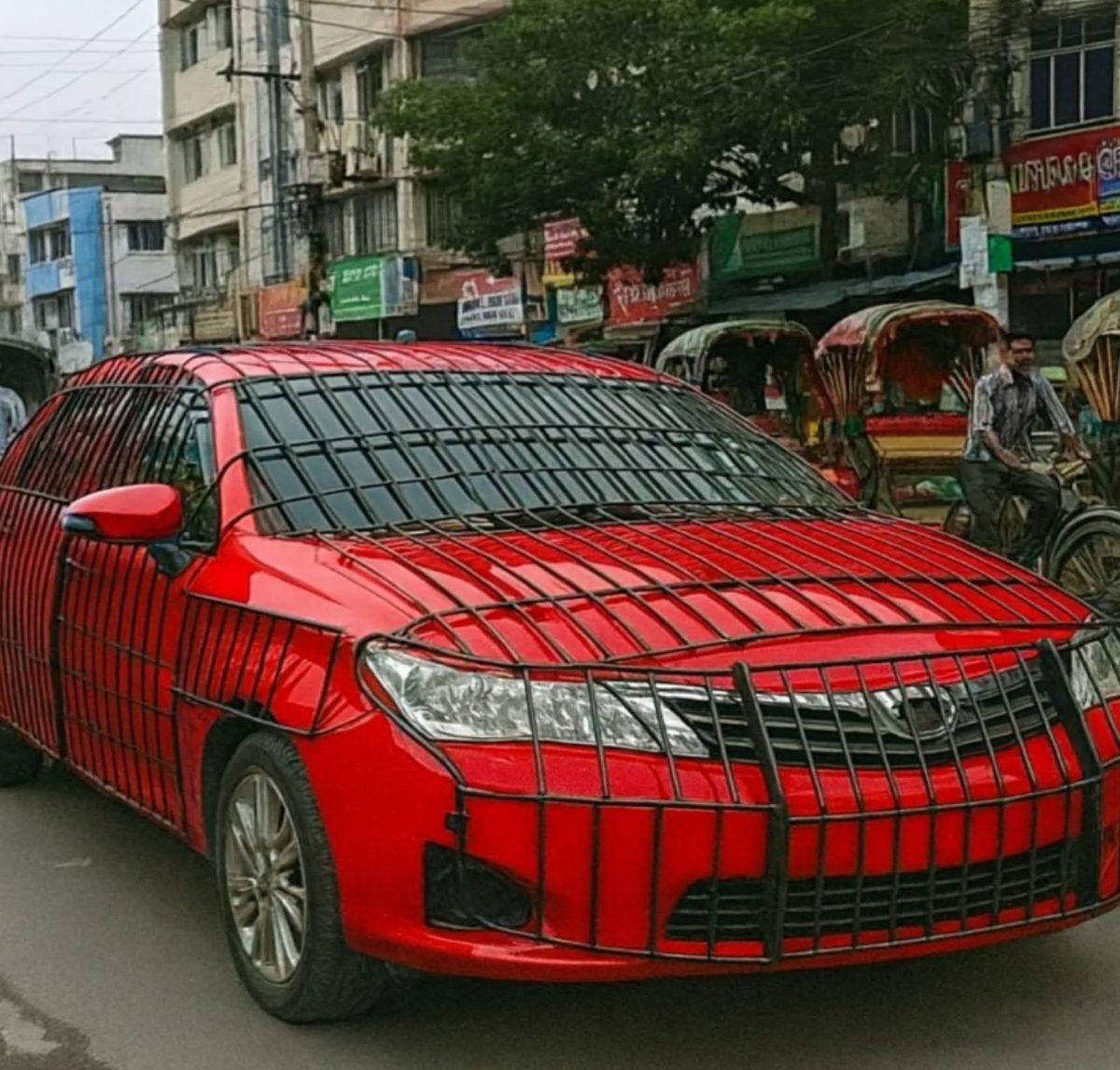 Červené auto s kovovou klietkou cez karosériu parkuje na rušnej ulici so staršími budovami a cyklistami.