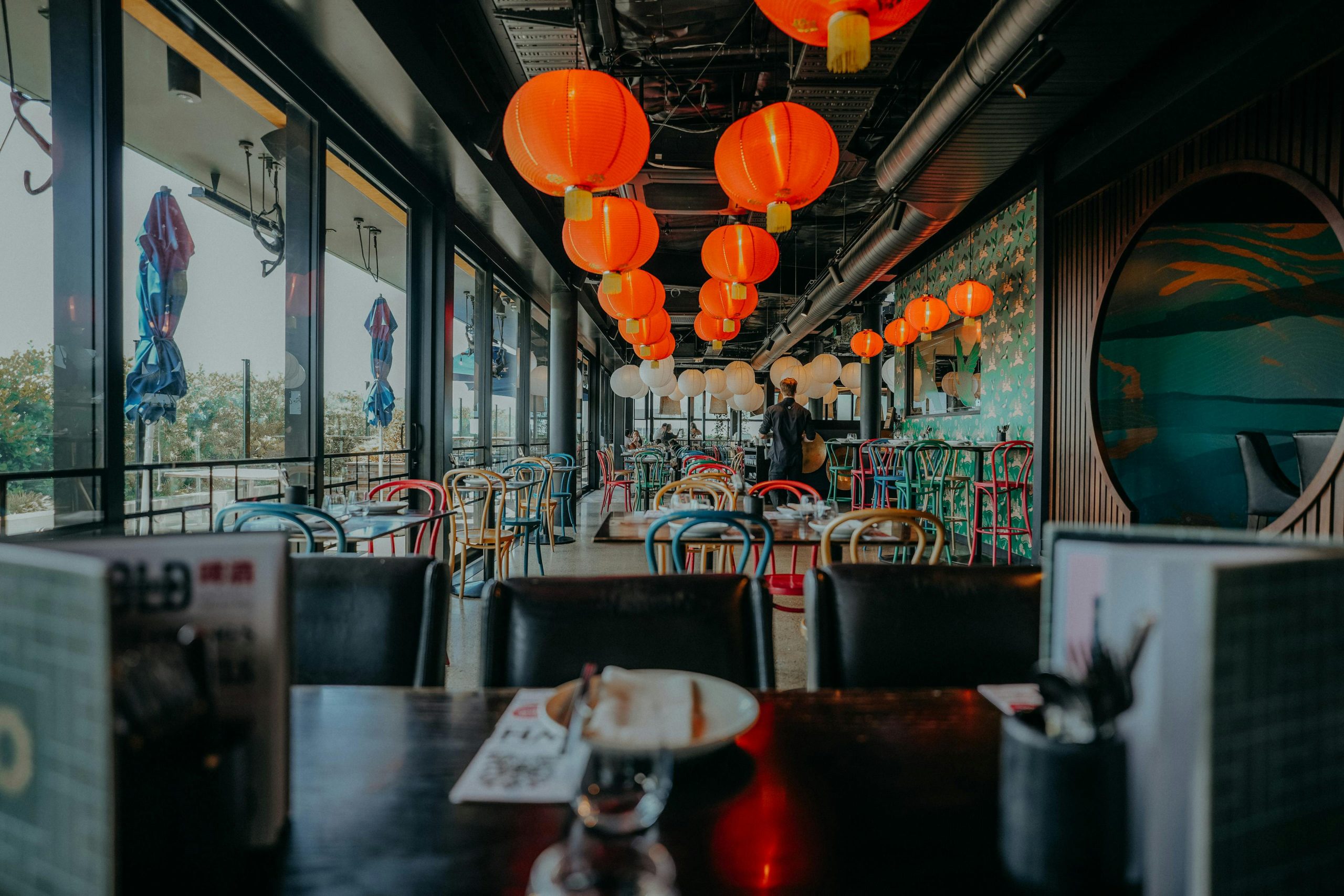 Moderná ázijská reštaurácia s farebnými stoličkami, lampiónmi a elegantnou atmosférou.