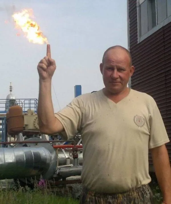 Osoba stojí pred priemyselným zariadením a ukazuje na oheň, ktorý vyzerá akoby vyšľahol z jej prsta.