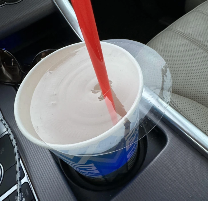 Pohár s čokoládovým nápojom a červenou slamkou v držiaku auta na nápoj, interiér vozidla.