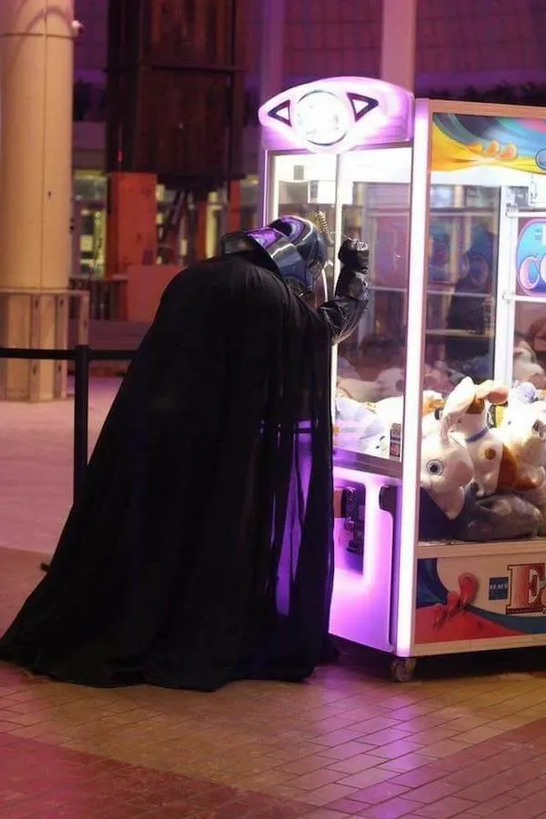 Neznáma postava v čiernom plášti hrá na automatoch s plyšovými hračkami v nákupnom centre.