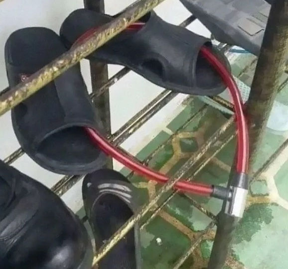 Čierne šľapky zabezpečené červeným zámkom na policovom regáli.