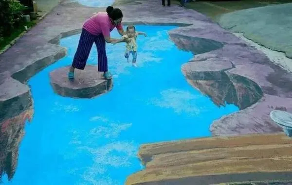 Matka a dieťa prechádzajú 3D ilúziou jazera na ulici, úchvatné umenie kriedou na chodníku.