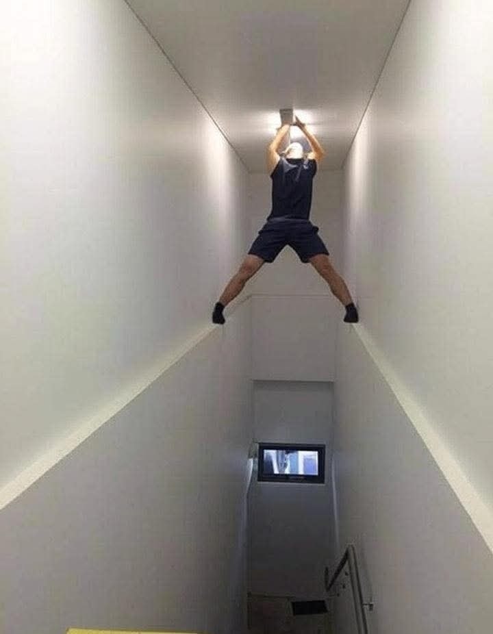 Osoba na schodoch opravuje svetlo zaujímavým spôsobom, stojac medzi stenami.