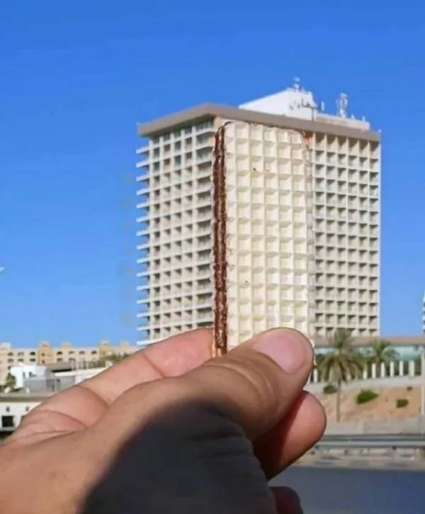 Osoba drží oplátku tak, aby pôsobila ako súčasť budovy v pozadí, čím vytvára optickú ilúziu.