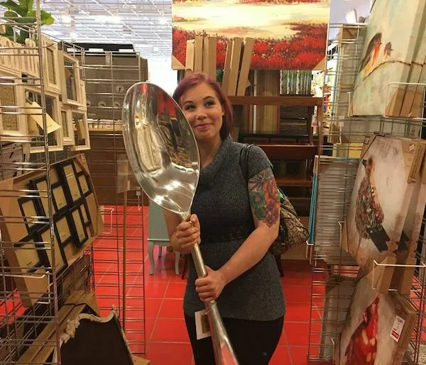 Žena s veľkou dekoratívnou lyžicou stojí v obchode s umeleckými dielami a obrazmi.