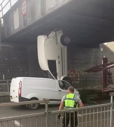 Dodávka prevrátená hore nohami pod nízkym mostom, policajt na mieste.