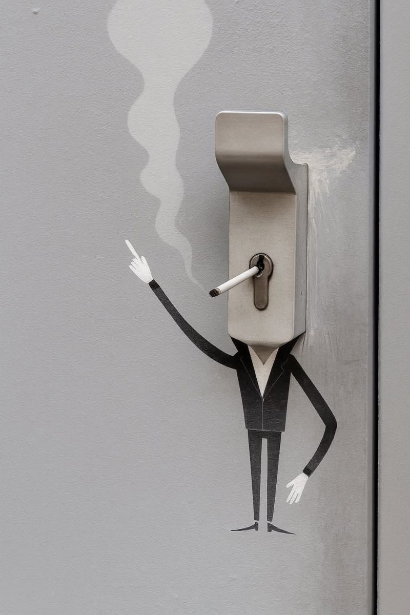 Vtipná nástenná maľba muža v obleku s kľúčovou dierkou ako tvárou, drží cigaretu, výraz umenia na sivých dverách.