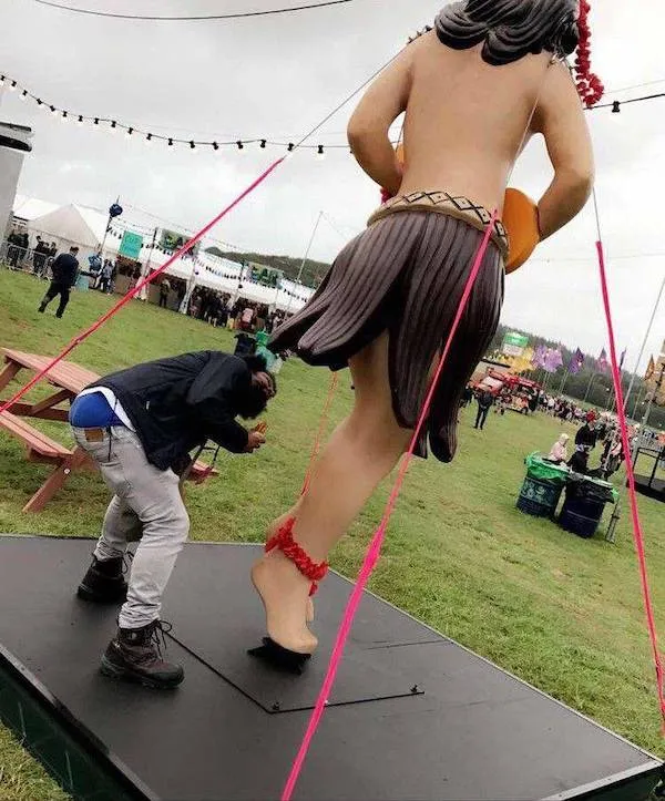 Osoba pózuje pri veľkej soške tanečníka na festivale pod šnúrami svetiel.