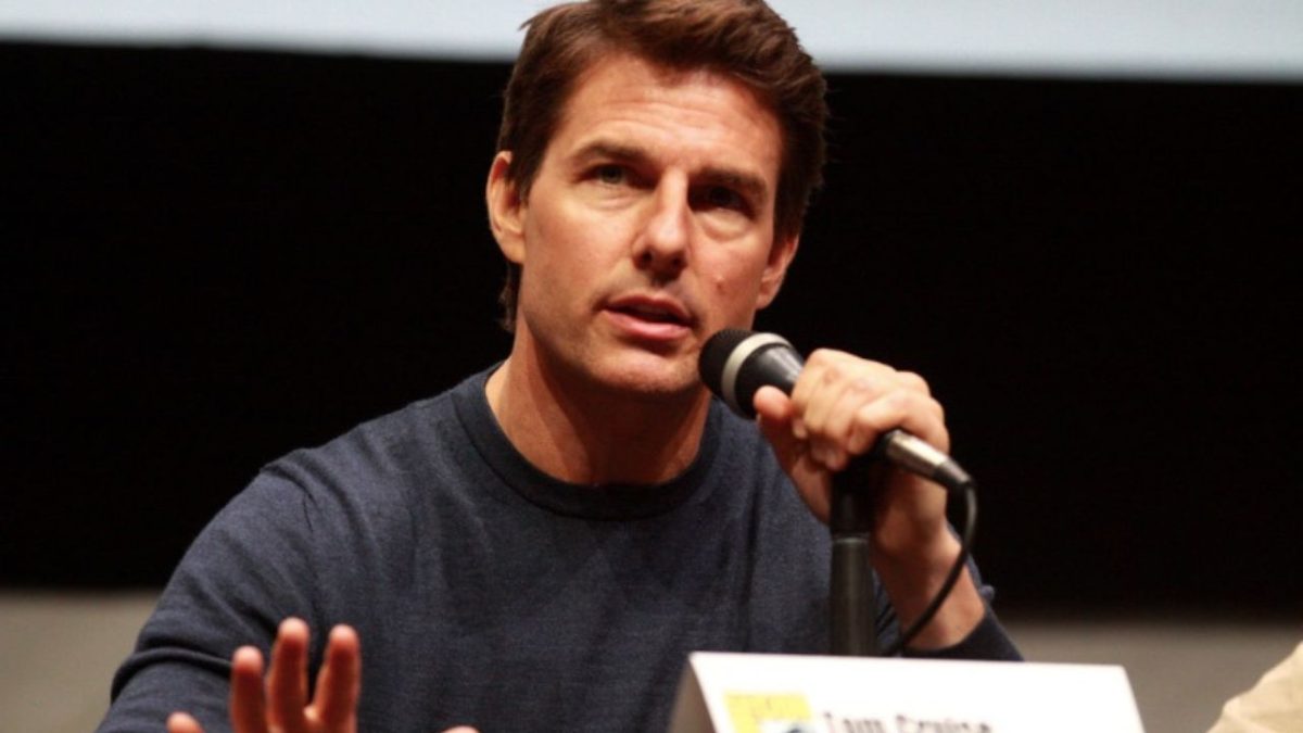 Osoba s mikrofónom rozpráva na verejnom podujatí, oblečená v tmavom svetri.