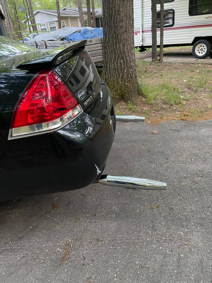 Auto so zdvojeným výfukom zaparkované v prírodnom prostredí s karavanom v pozadí.