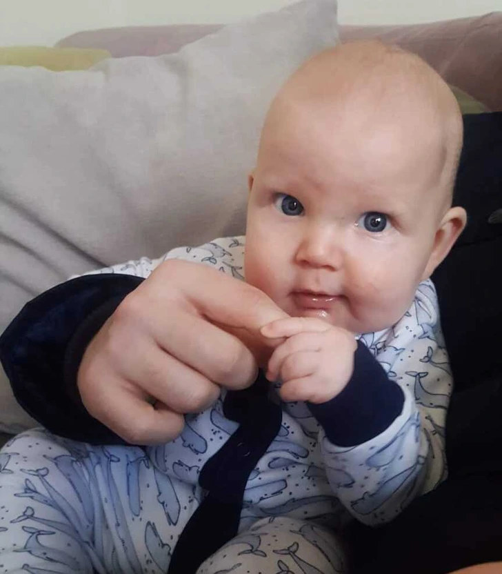 Bábätko v pyžamku drží dospelú ruku, pozera sa s veľkými očami.