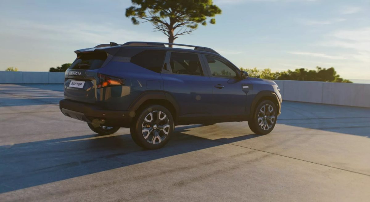 Modré SUV parkuje na slnkom zaliatej ploche, v pozadí je strom, jasná obloha a stromy.