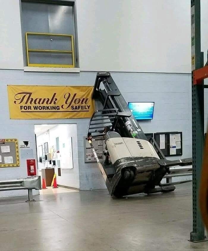 Vysokozdvižný vozík zablokovaný vo vchode pod transparentom o bezpečnosti práce.