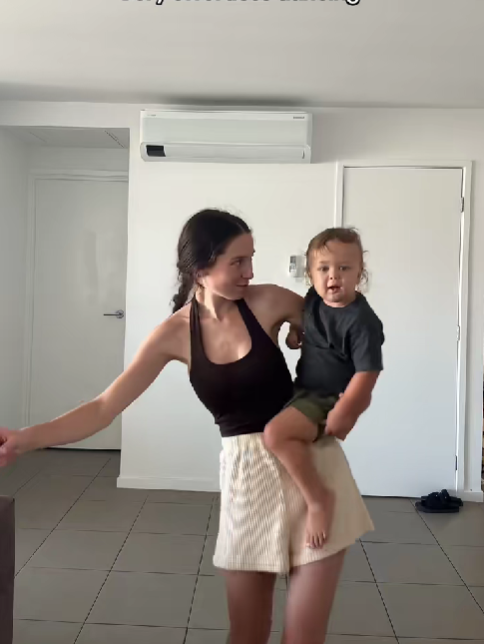 Žena v čiernom tielku drží dieťa na ruke v modernom interiéri bytu.