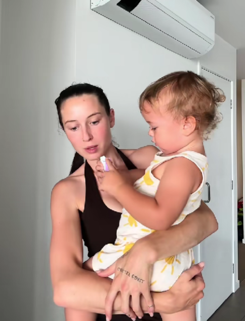 Mladá žena v športovom oblečení drží malé dieťa v náručí v interiéri.