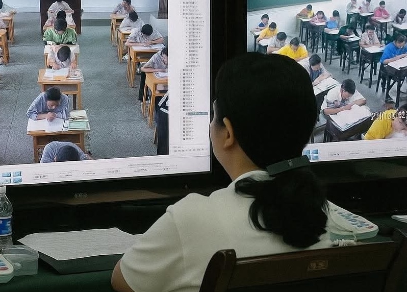 Osoba sledujúca študentov cez monitor počas skúšky v triede.