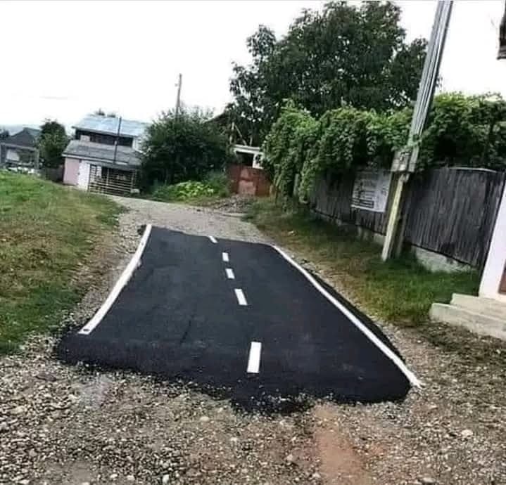 Nedokončená asfaltová cesta vedúca z domu na nespevnený povrch v prirodzenom prostredí vidieka.