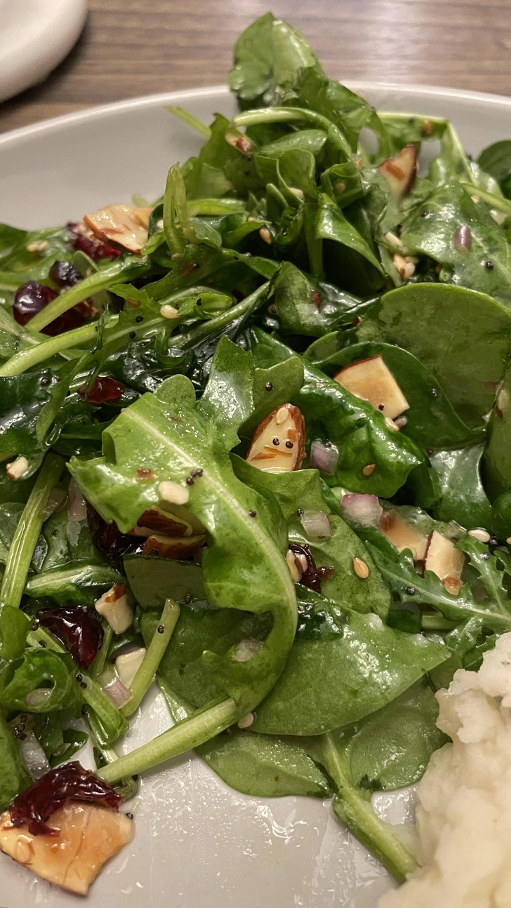 Čerstvý špenátový šalát s mandľami, brusnicami a zálievkou na tanieri, ideálny pre zdravú stravu.