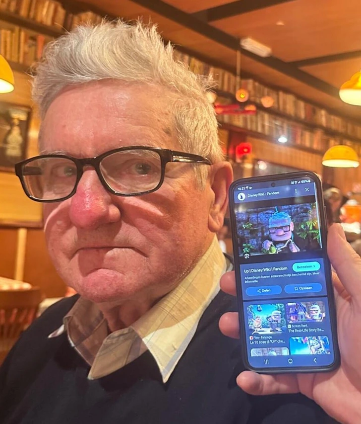 Starší muž na fotografii drží telefón s obrázkom animovanej postavy z filmu.