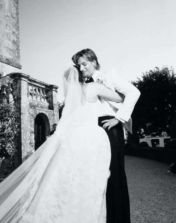 Svadobný pár v objatí pred historickou budovou, nevesta v dlhej závoji, čiernobiela fotografia.