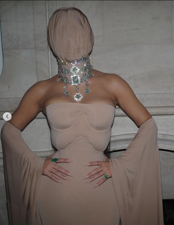 Elegantný outfit s telovým závojom a lesklým náhrdelníkom na spoločenskej akcii.