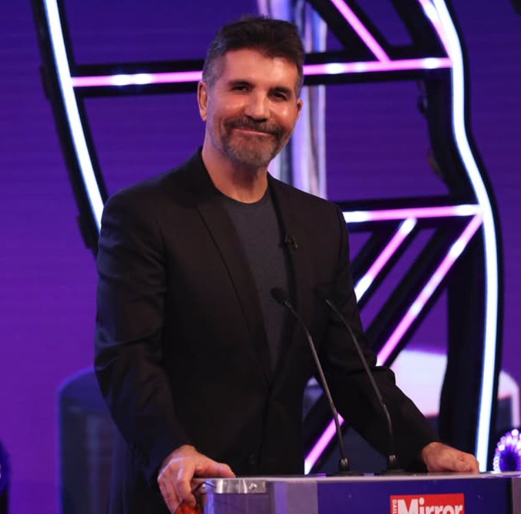 Osoba stojí na pódiu s mikrofónom pred moderným farebným pozadím na verejnej akcii.