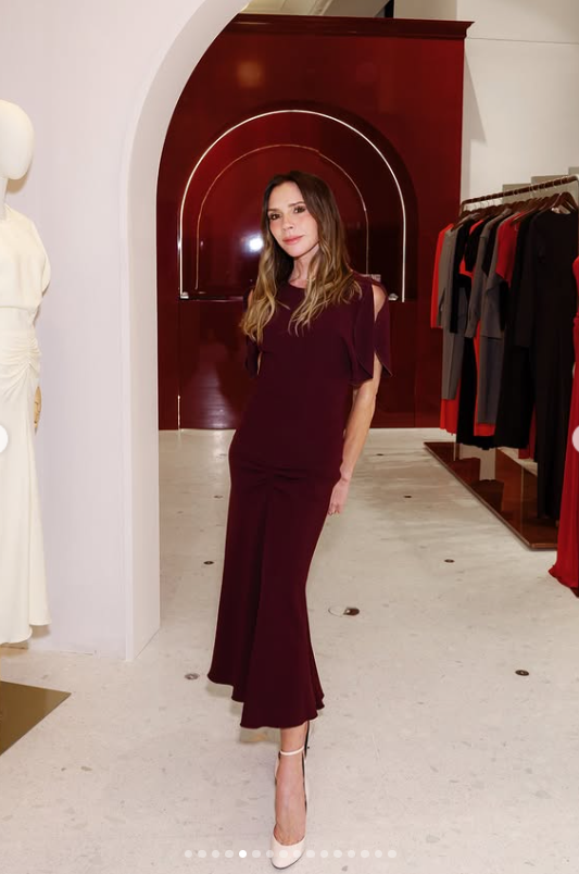 Osoba v elegantných šatách stojí v módnom butiku s oblúkovým vstupom a vystavenými šatami v pozadí.