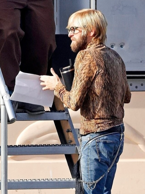 Osoba s fúzami a okuliarmi stojí na schodoch, drží dokument a termo hrnček.