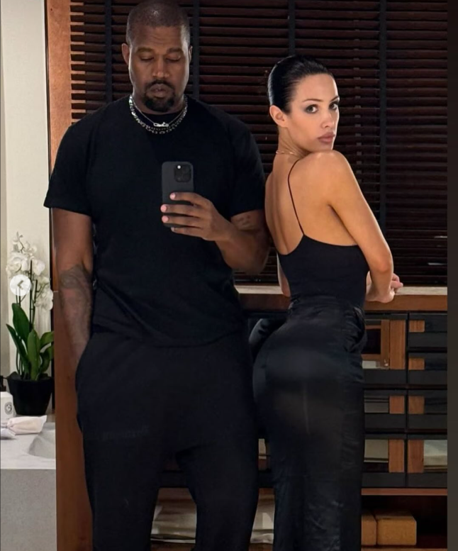 Dvaja ľudia v čiernom oblečení pózujú pred zrkadlom v interiéri.