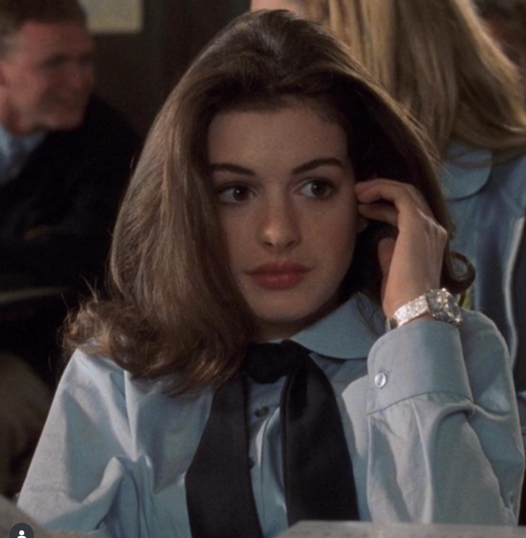 Mladá žena v uniforme sedí v triede, dotýka sa vlasov a pozerá do diaľky.