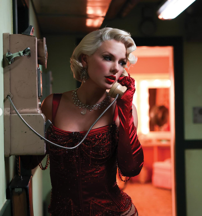 Žena v červenej róbe telefonuje na klasickom telefóne, elegantne oblečená s retro účesom.