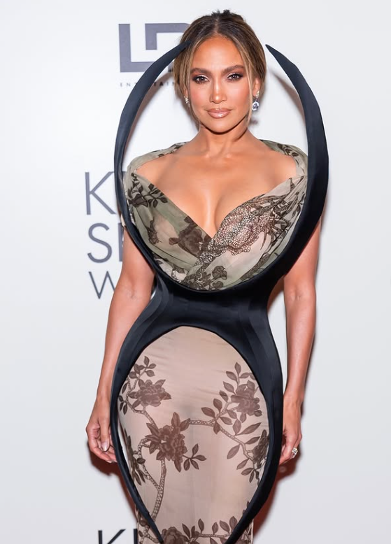 Osoba v elegantných šatách s kvetinovým vzorom pózuje na módnej udalosti.