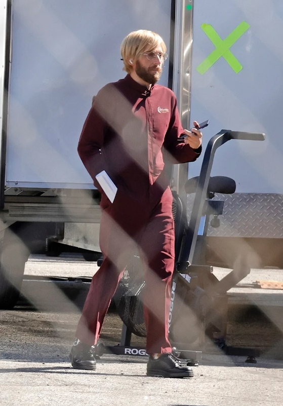 Osoba v červenom odeve kráča vedľa kamiónu a drží telefón, s knihou pod pažou.